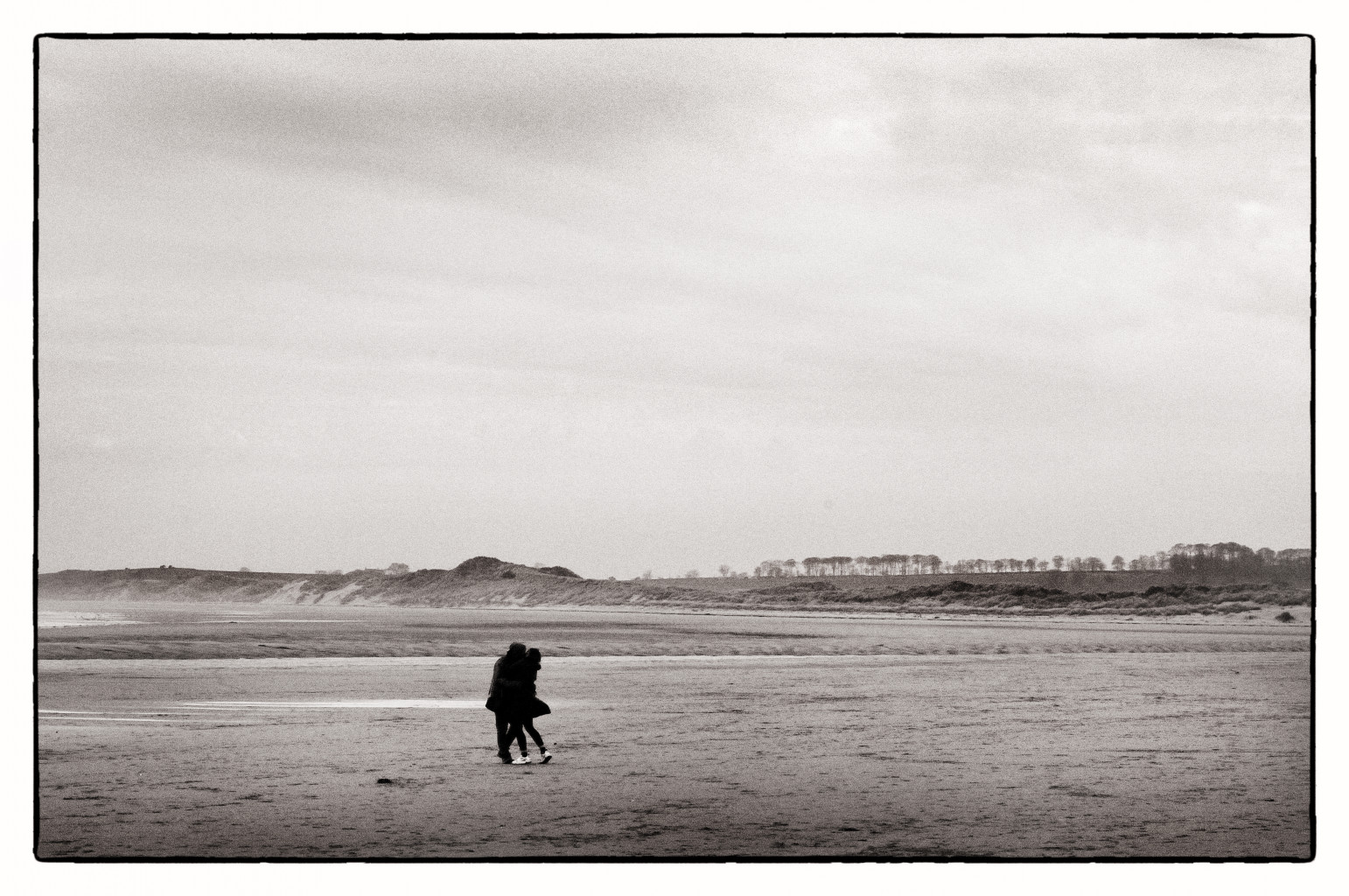 A couple embrace on an empty beach at Alnmouth in Northumberland.